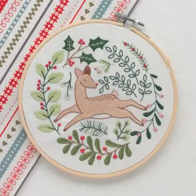 Image show an Christmas embroidery kit with a deer surrounded by greenery