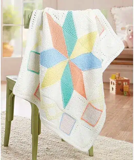 Showing a beautiful baby blanket with a large quilt inspired star on it. The blanket is knit in light pastels.